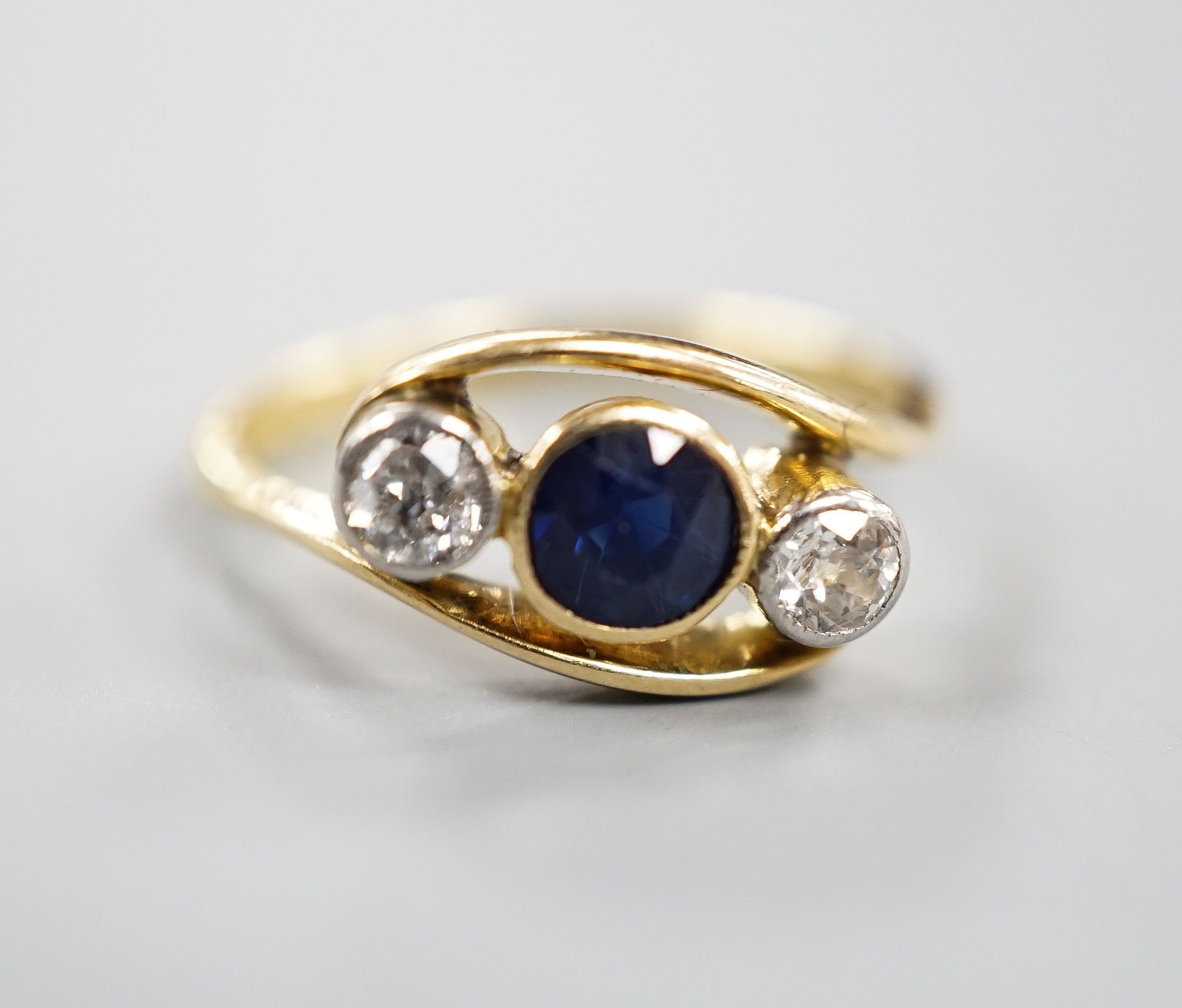 A modern 18ct gold, single stone diamond and two sapphire set crossover ring, size K, gross 3.2 grams.